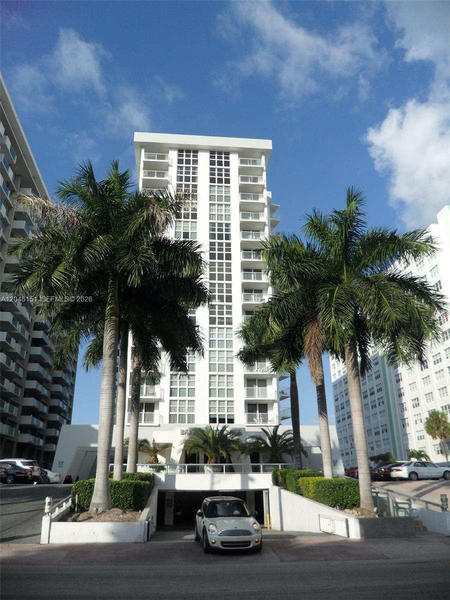 A white high-rise apartment building stands behind two palm trees and a parking garage entrance — 1228 West Ave # 1104, Miami Beach FL 33139, MIAMI BEACH, FL