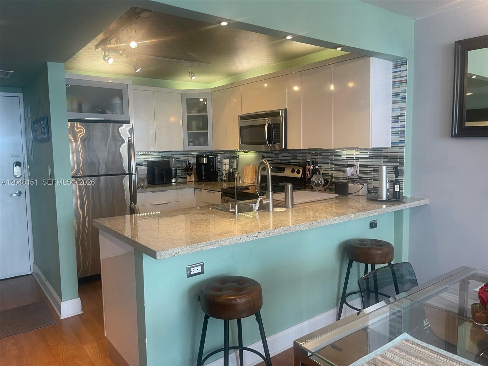 A kitchen features light-colored cabinets, granite countertops, a breakfast bar, and teal-painted walls — 1228 West Ave # 1104, Miami Beach FL 33139, MIAMI BEACH, FL