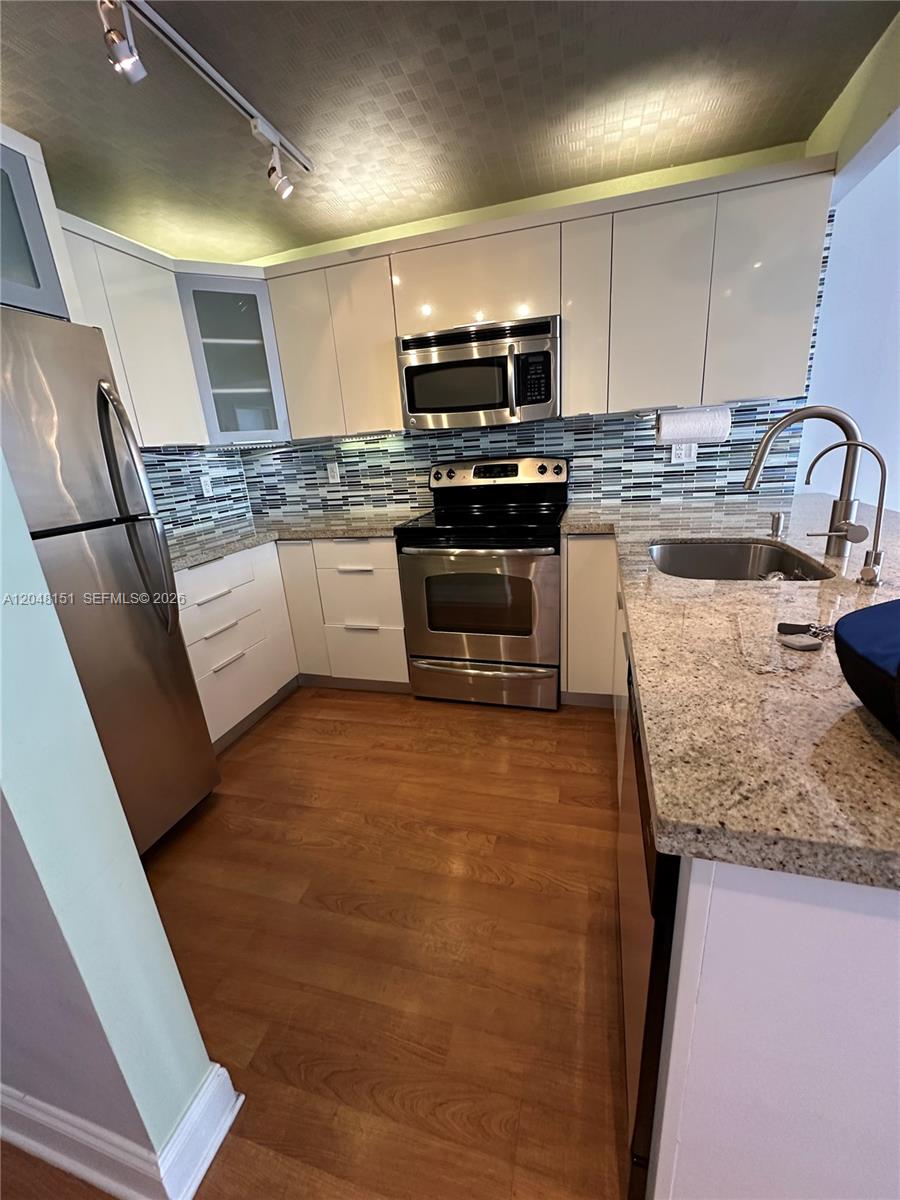 A kitchen features white cabinets, stainless steel appliances, granite countertops, and wood-look flooring — 1228 West Ave # 1104, Miami Beach FL 33139, MIAMI BEACH, FL