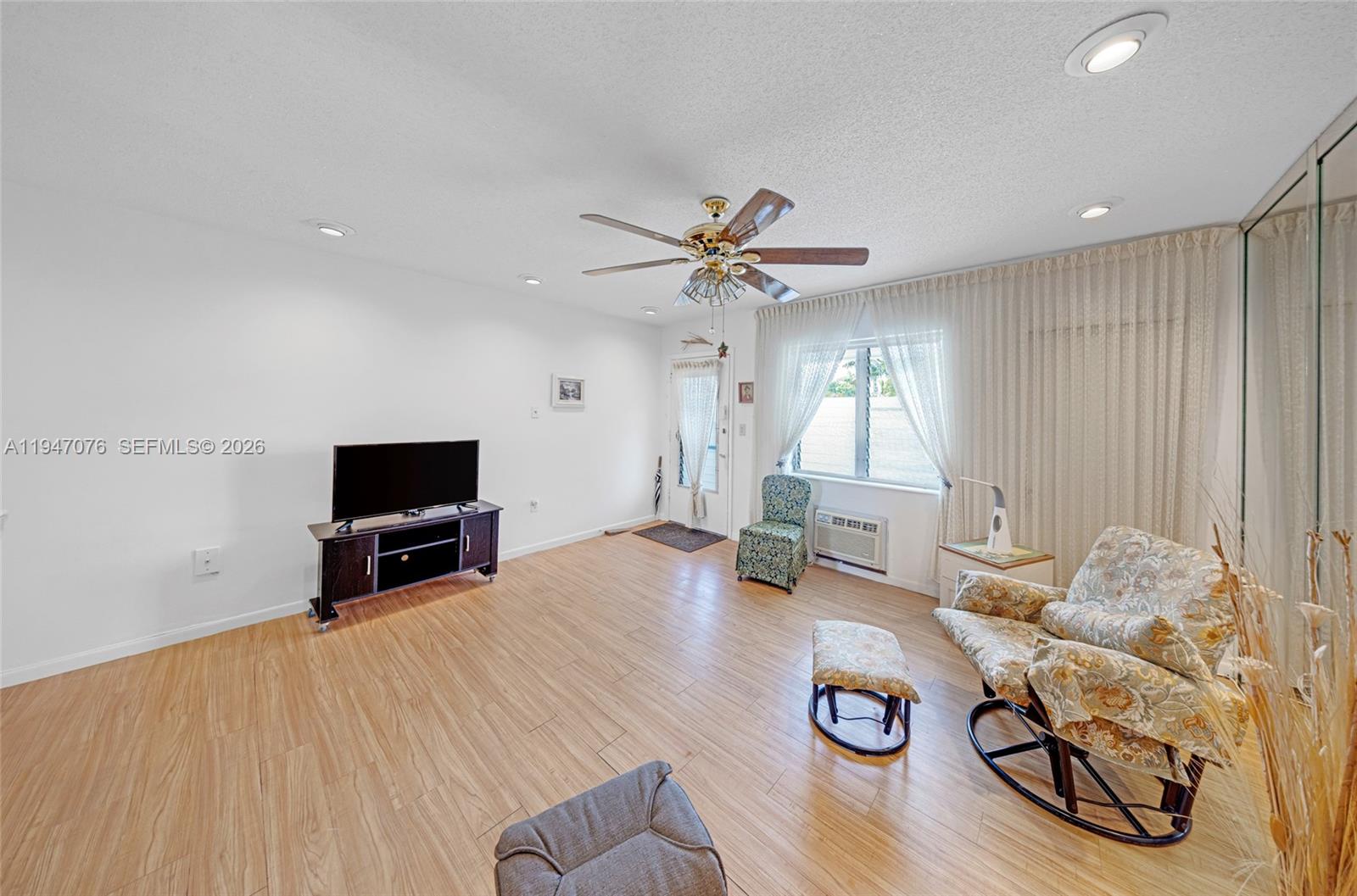 This living room features light wood-look flooring, a ceiling fan, and a floral armchair — 15600 NE 6th Ave # 28D, Miami FL 33162, MIAMI, FL