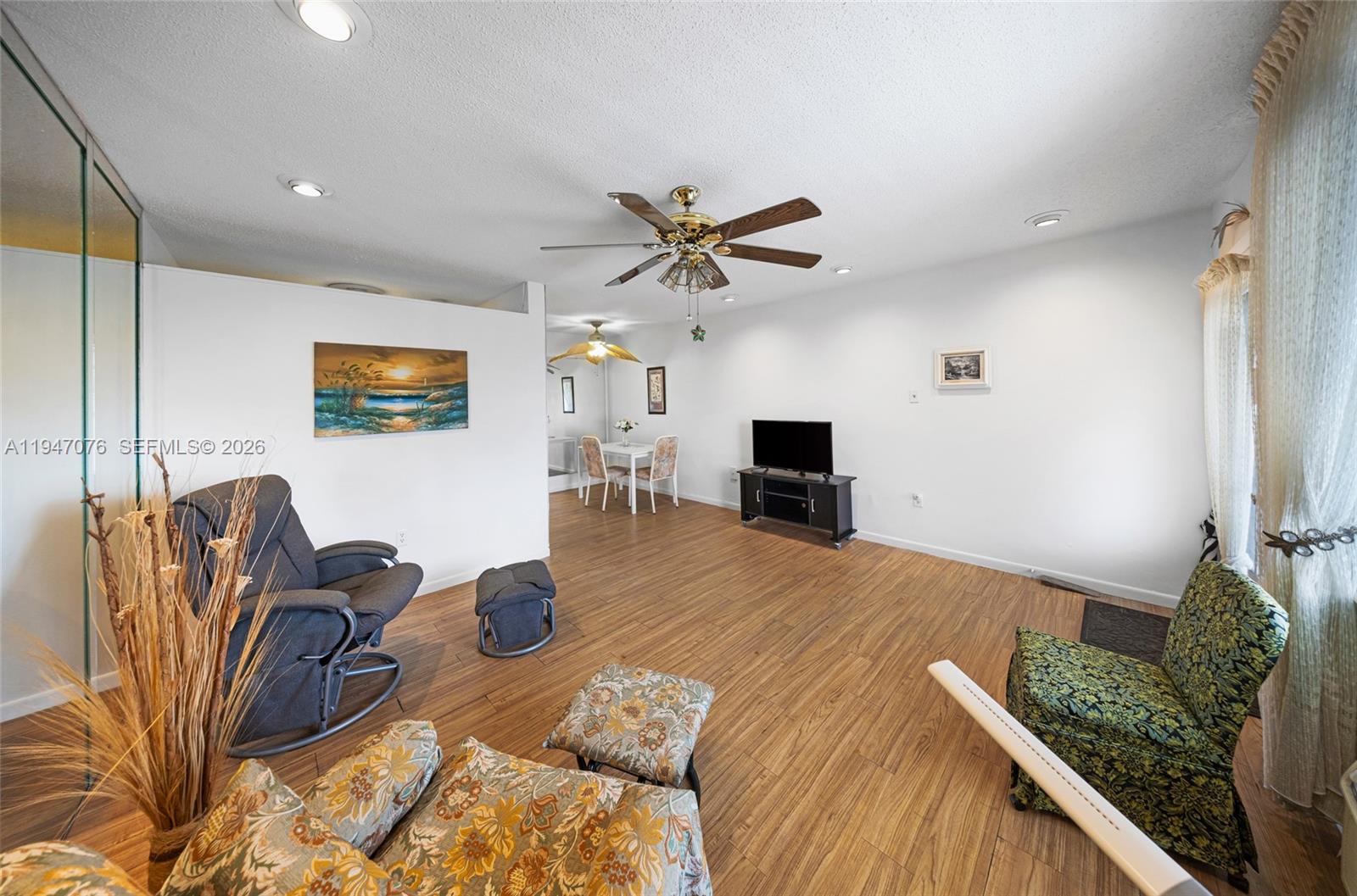 A living room features wood-look flooring, white walls, a ceiling fan, and a dining area — 15600 NE 6th Ave # 28D, Miami FL 33162, MIAMI, FL