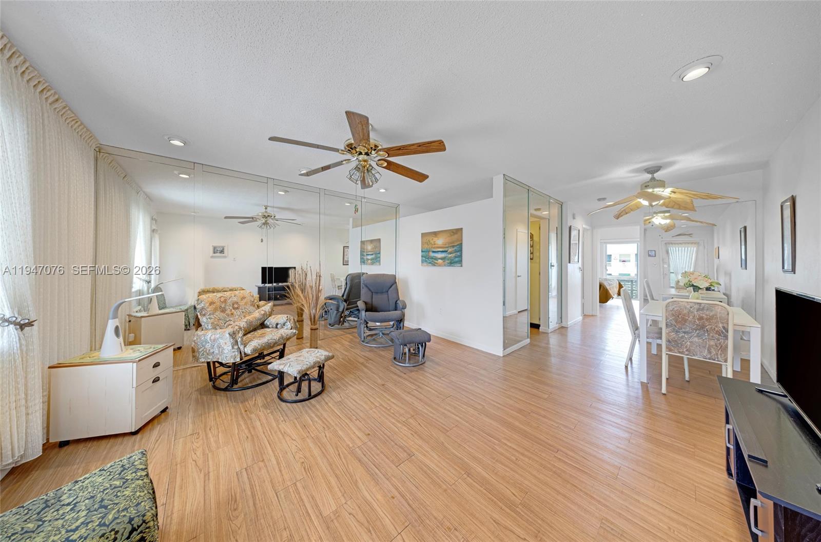 A living and dining area features wood-look flooring, mirrored walls, and ceiling fans — 15600 NE 6th Ave # 28D, Miami FL 33162, MIAMI, FL