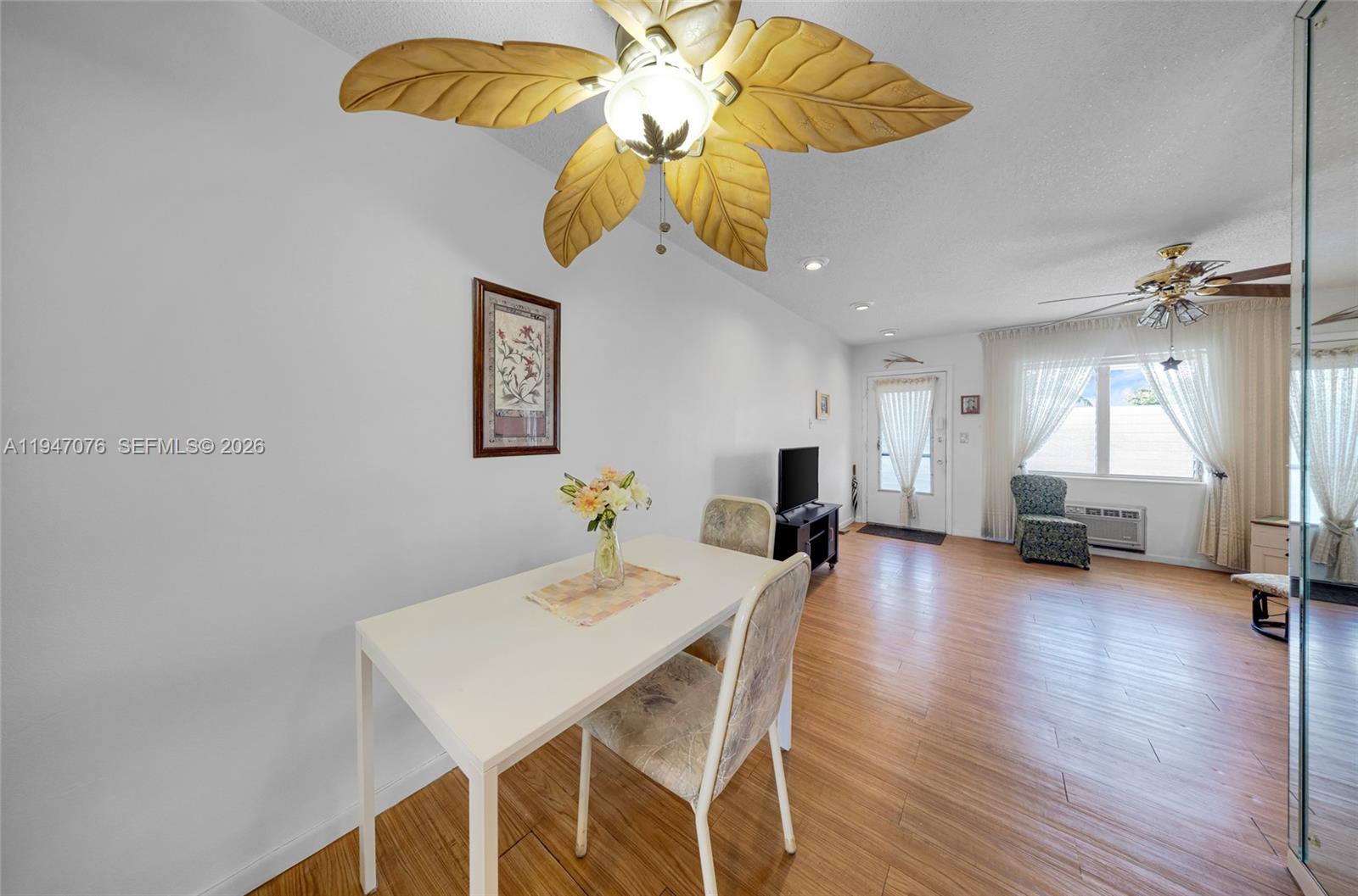 A dining area with a leaf-shaped ceiling fan, white table, and wood-look flooring — 15600 NE 6th Ave # 28D, Miami FL 33162, MIAMI, FL
