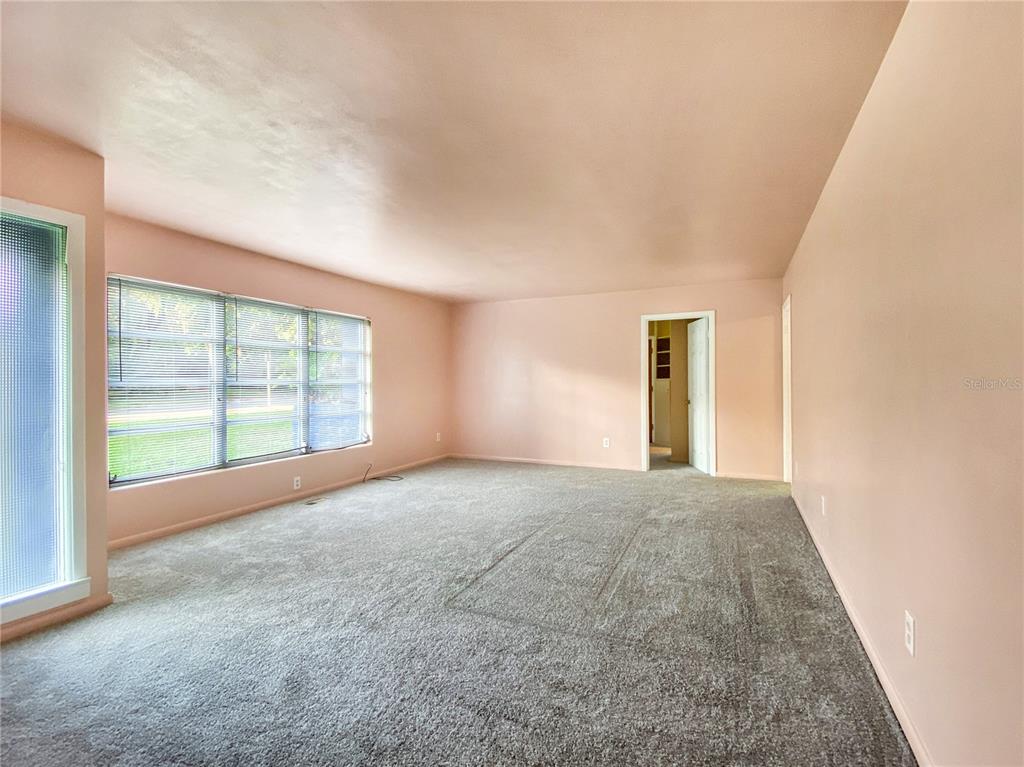 A living room with light pink walls, gray carpeting, and a large window with blinds — 1119 SW 11TH AVENUE, GAINESVILLE, FL