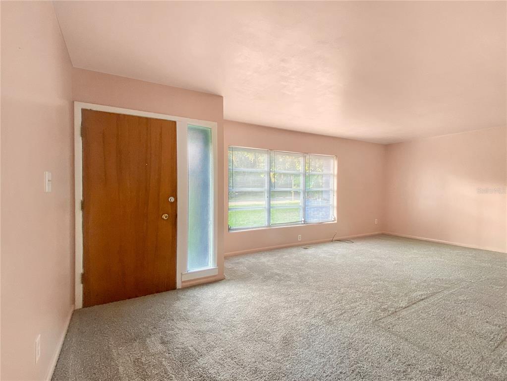 A living room with pink walls, gray carpeting, a wooden front door, and large windows — 1119 SW 11TH AVENUE, GAINESVILLE, FL