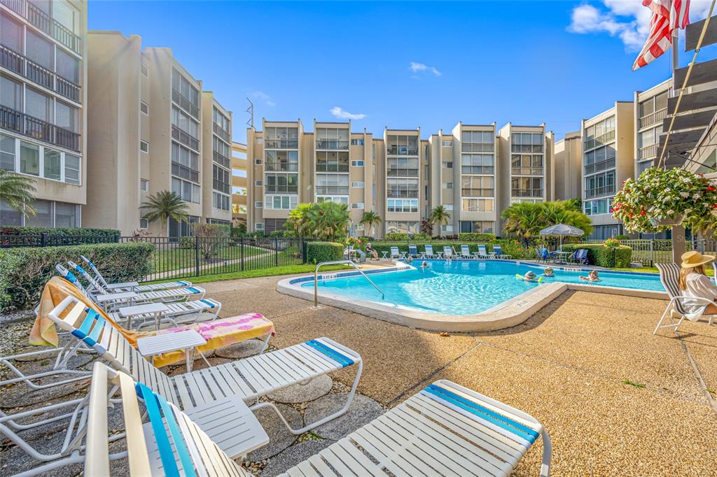 A swimming pool surrounded by lounge chairs sits in the courtyard of a multi-story apartment building — 1243 S MARTIN LUTHER KING JR AVENUE UNIT C505, CLEARWATER, FL