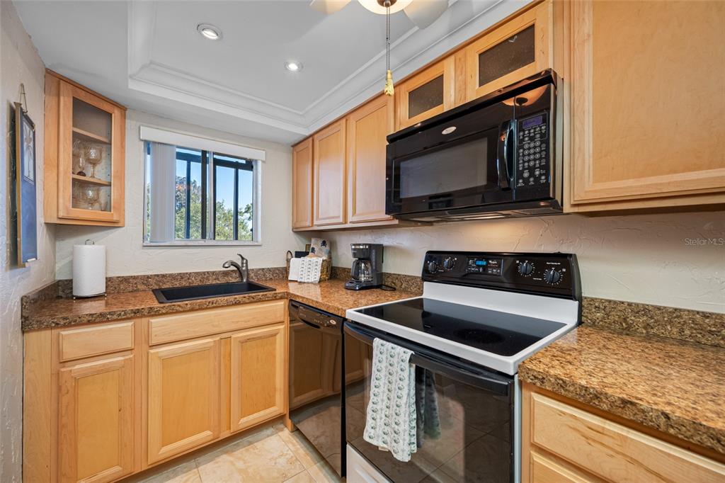 A kitchen features light wood cabinets, granite countertops, and black appliances — 1243 S MARTIN LUTHER KING JR AVENUE UNIT C505, CLEARWATER, FL