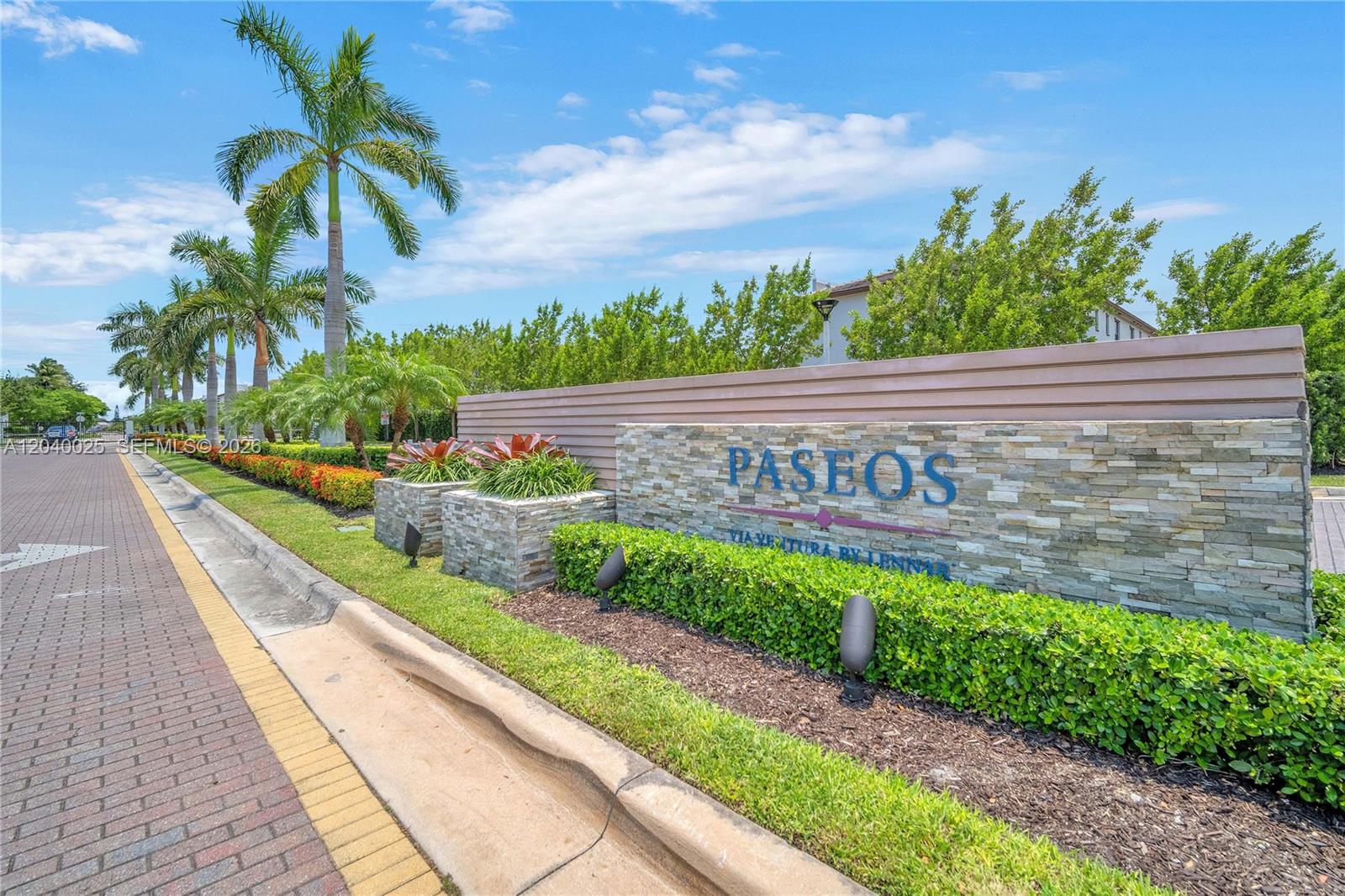 A stone monument sign for Paseos stands beside a brick road and palm trees — 670 NE 207th St, Miami FL 33179, MIAMI, FL