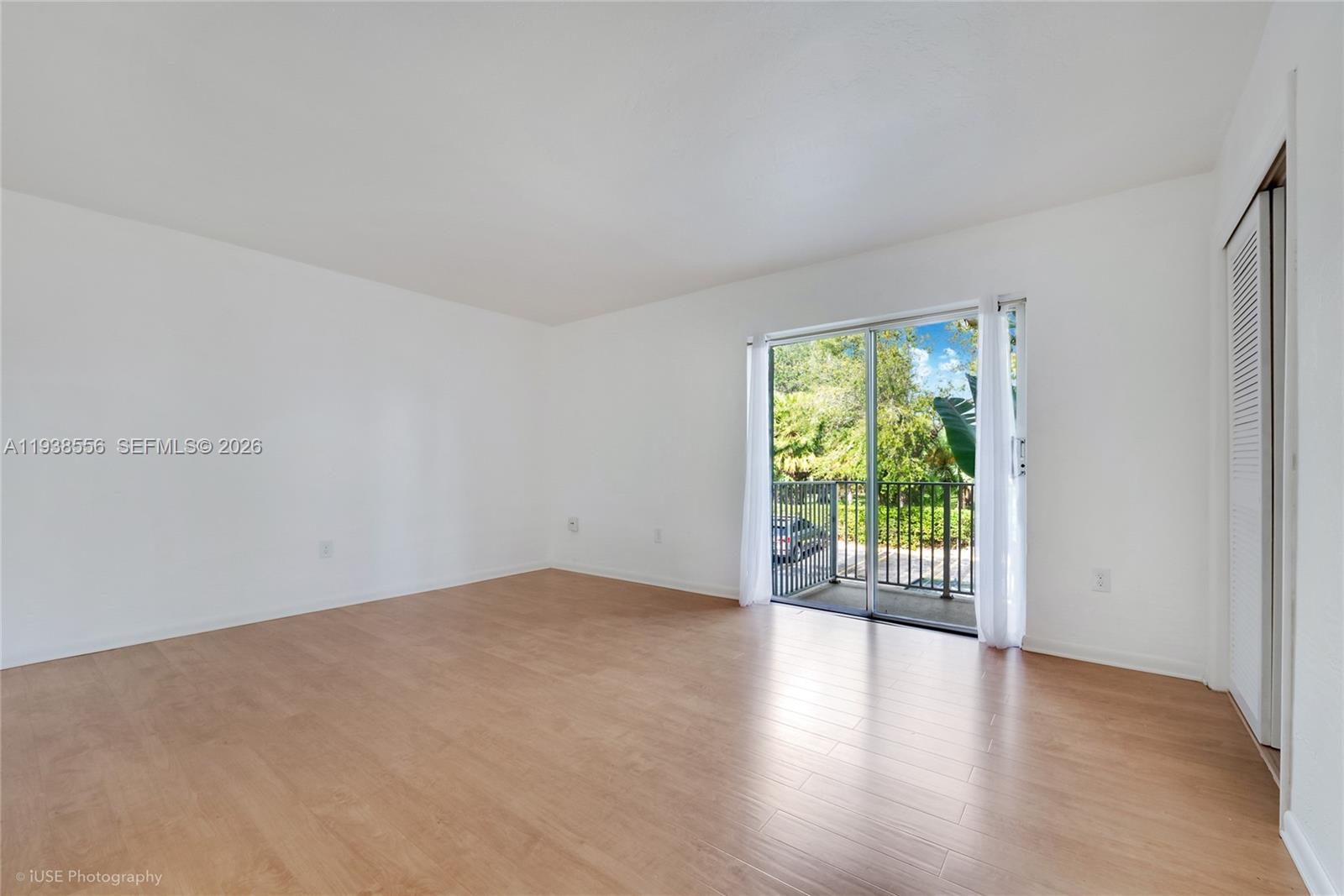 An empty room features light wood-look flooring, white walls, and a sliding glass balcony door — 7403 SW 82nd St # 210N, Miami FL 33143, MIAMI, FL