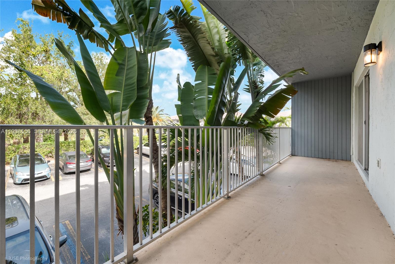 A covered balcony overlooks a parking lot with large tropical plants growing near the railing — 7403 SW 82nd St # 210N, Miami FL 33143, MIAMI, FL