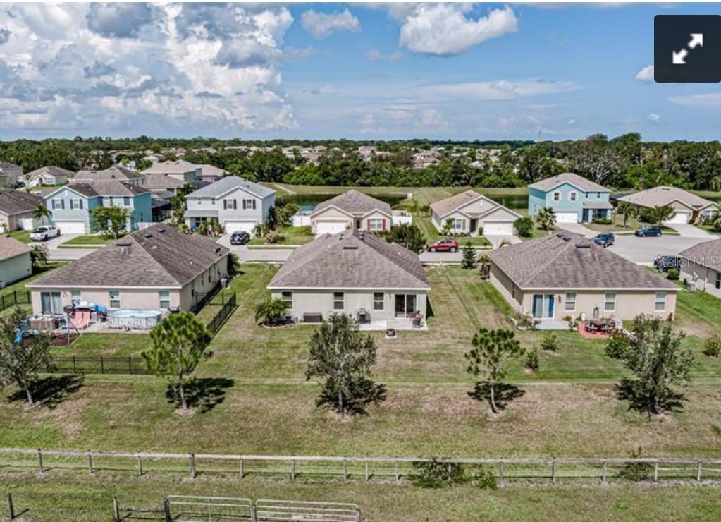 An aerial view shows the backyards of three suburban houses with a fenced pasture behind — 7114 58TH TERRACE E, PALMETTO, FL