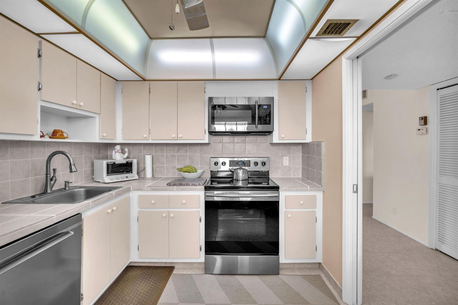 A kitchen features light-colored cabinets, stainless steel appliances, tiled countertops, and a tray ceiling — 605 Oaks Drive # 907, Pompano Beach FL 33069, POMPANO BEACH, FL