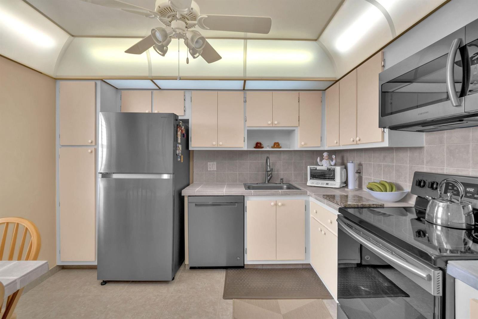 A kitchen features light-colored cabinets, stainless steel appliances, a tiled backsplash, and a ceiling fan — 605 Oaks Drive # 907, Pompano Beach FL 33069, POMPANO BEACH, FL