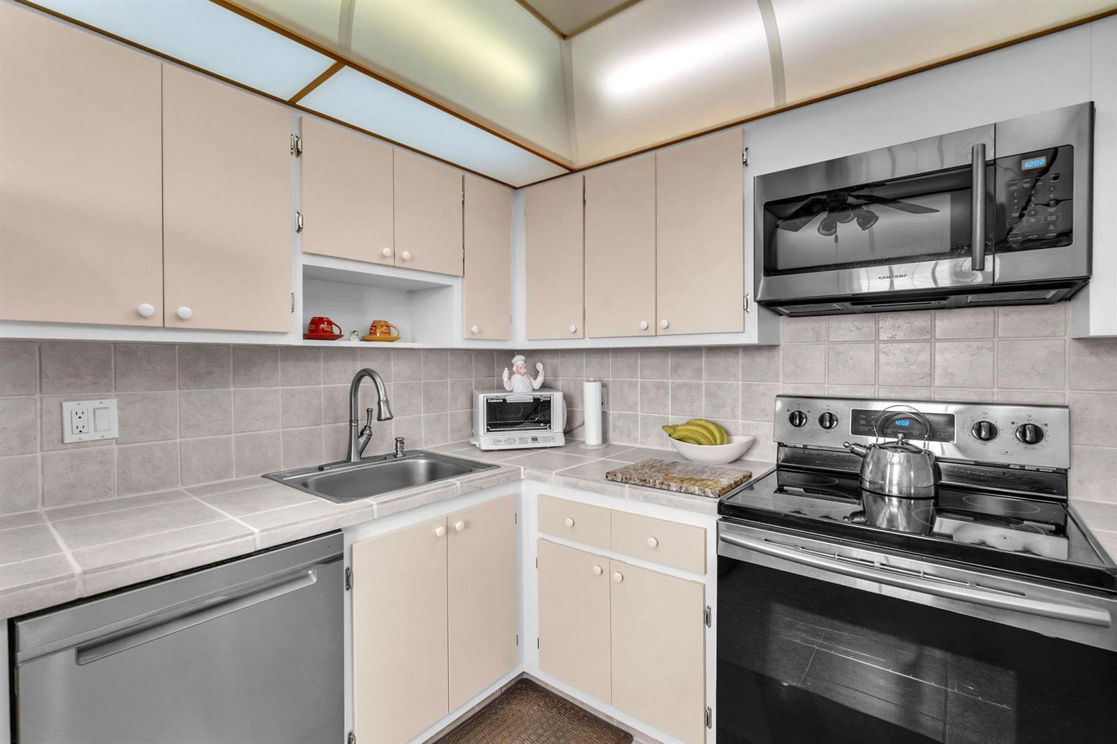 A kitchen features light-colored cabinets, tiled countertops, stainless steel appliances, and a tiled backsplash — 605 Oaks Drive # 907, Pompano Beach FL 33069, POMPANO BEACH, FL