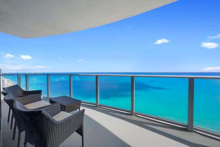 A balcony with wicker chairs overlooks a vast blue ocean under a clear sky — 4111 S Ocean Dr # 3002, Hollywood FL 33019, HOLLYWOOD, FL