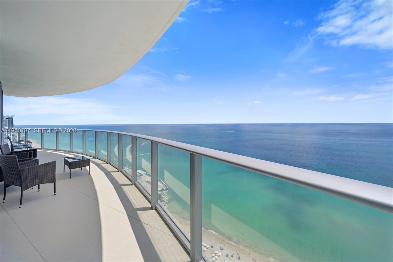 A curved balcony with glass railings overlooks the ocean and a sandy beach below — 4111 S Ocean Dr # 3002, Hollywood FL 33019, HOLLYWOOD, FL