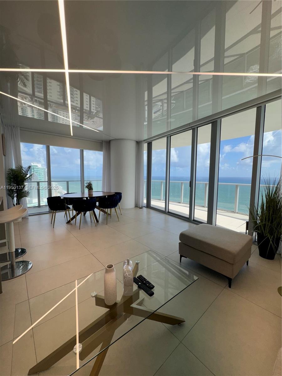 A modern living and dining area features floor-to-ceiling windows with ocean views and tiled floors — 4111 S Ocean Dr # 3002, Hollywood FL 33019, HOLLYWOOD, FL