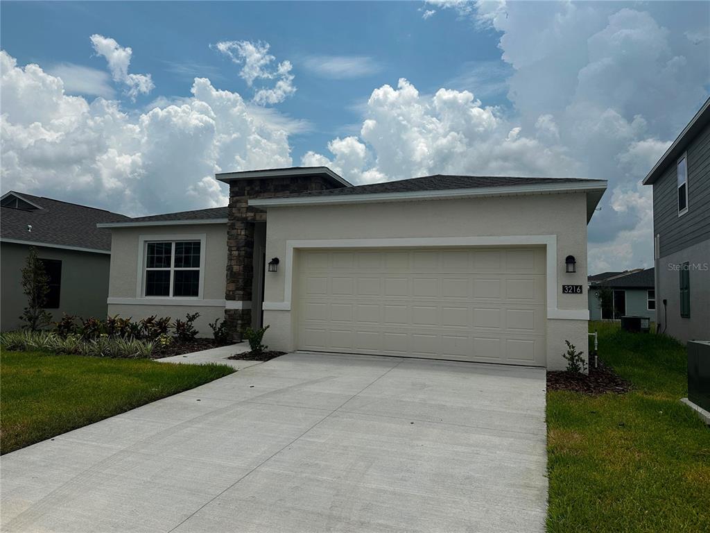 A single-story house with a beige stucco exterior, stone accents, and a two-car garage — 3216 ALPINE WAY, DAVENPORT, FL