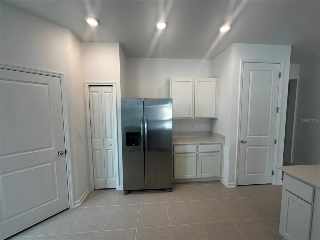 A kitchen features white cabinets, a stainless steel refrigerator, and tiled flooring — 3216 ALPINE WAY, DAVENPORT, FL