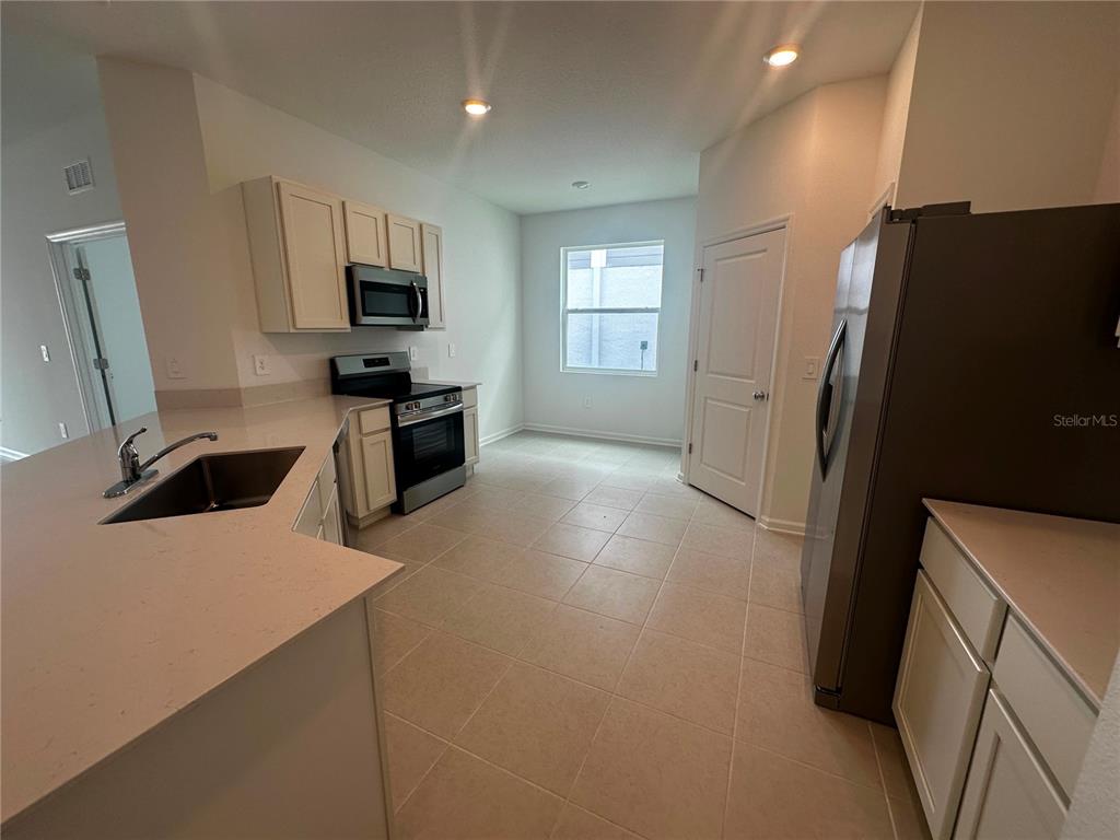 A kitchen features light-colored cabinets, stainless steel appliances, a corner sink, and tile flooring — 3216 ALPINE WAY, DAVENPORT, FL