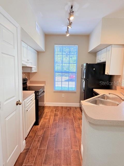 A kitchen features white cabinets, wood-look tile flooring, a window, and a black refrigerator — 9108 LAKE CHASE ISLAND WAY UNIT 9108, TAMPA, FL