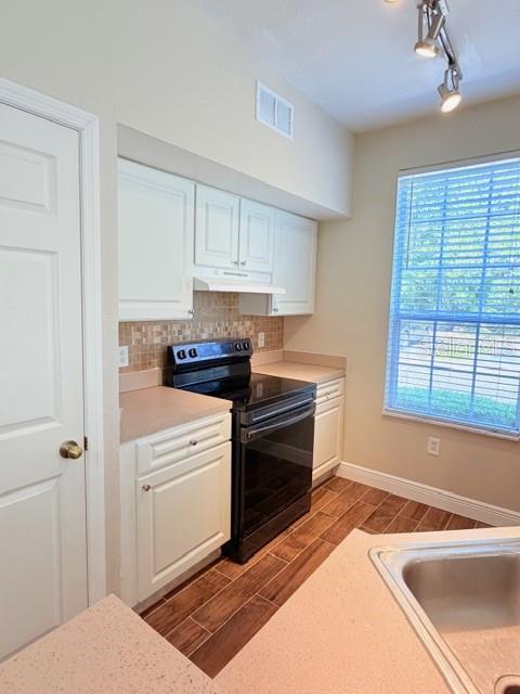 A kitchen features white cabinets, a black stove, a tiled backsplash, and wood-look flooring — 9108 LAKE CHASE ISLAND WAY UNIT 9108, TAMPA, FL