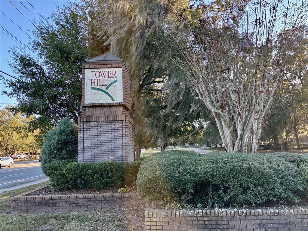 A brick monument sign for Tower Hill stands beside a road with trees and landscaping — 230 NW 76TH DRIVE UNIT B, GAINESVILLE, FL