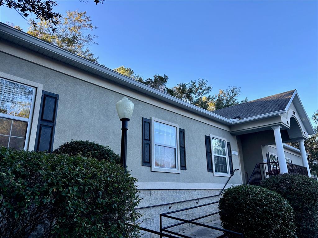 A low-angle exterior view of a building with stucco walls, dark shutters, and a ramp — 230 NW 76TH DRIVE UNIT B, GAINESVILLE, FL