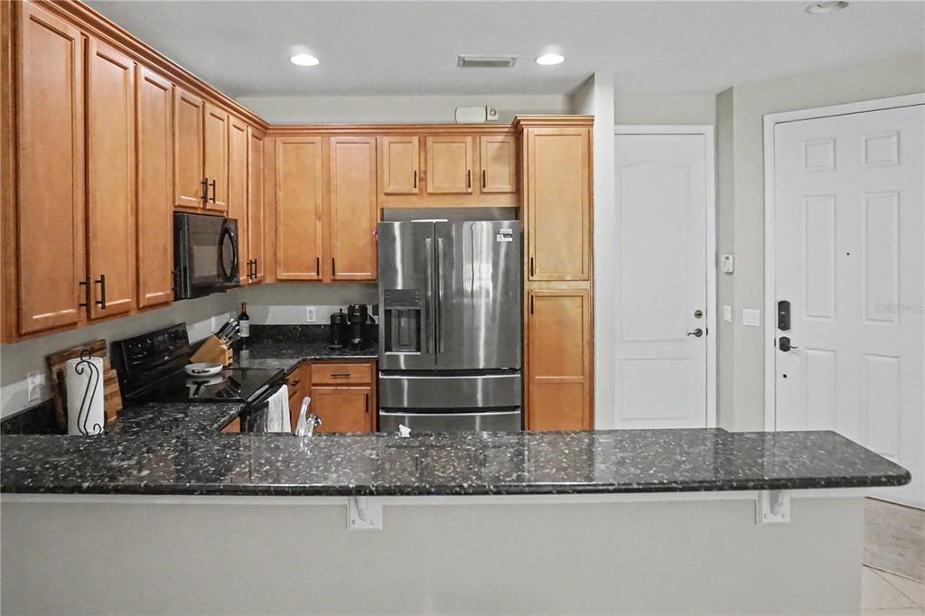 A kitchen features wood cabinets, dark granite countertops, stainless steel appliances, and a breakfast bar — 1828 GARDEN SAGE DRIVE, OVIEDO, FL