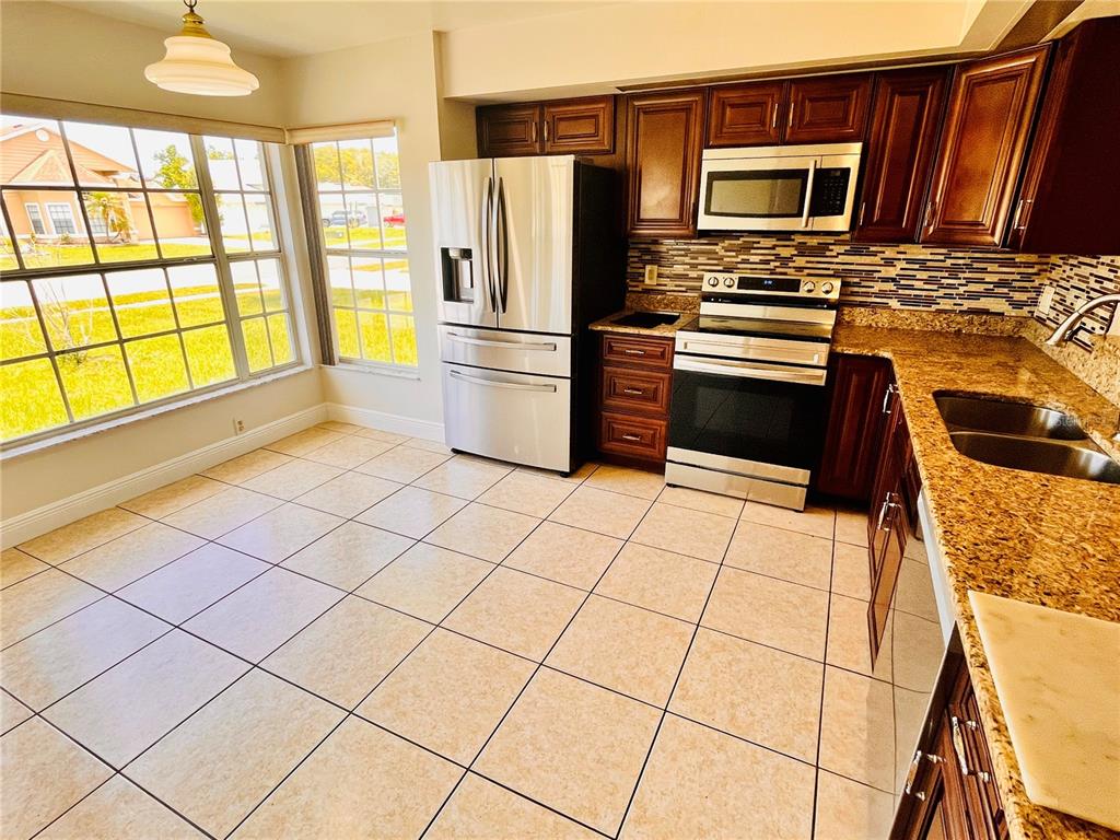 A kitchen with dark wood cabinets, granite countertops, stainless steel appliances, and tile flooring — 13534 TEXAS WOODS CIRCLE, ORLANDO, FL