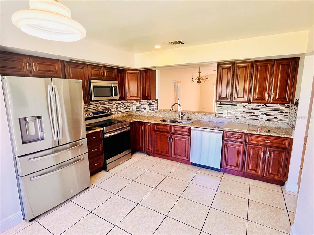 A kitchen with dark wood cabinets, stainless steel appliances, granite countertops, and tiled flooring — 13534 TEXAS WOODS CIRCLE, ORLANDO, FL