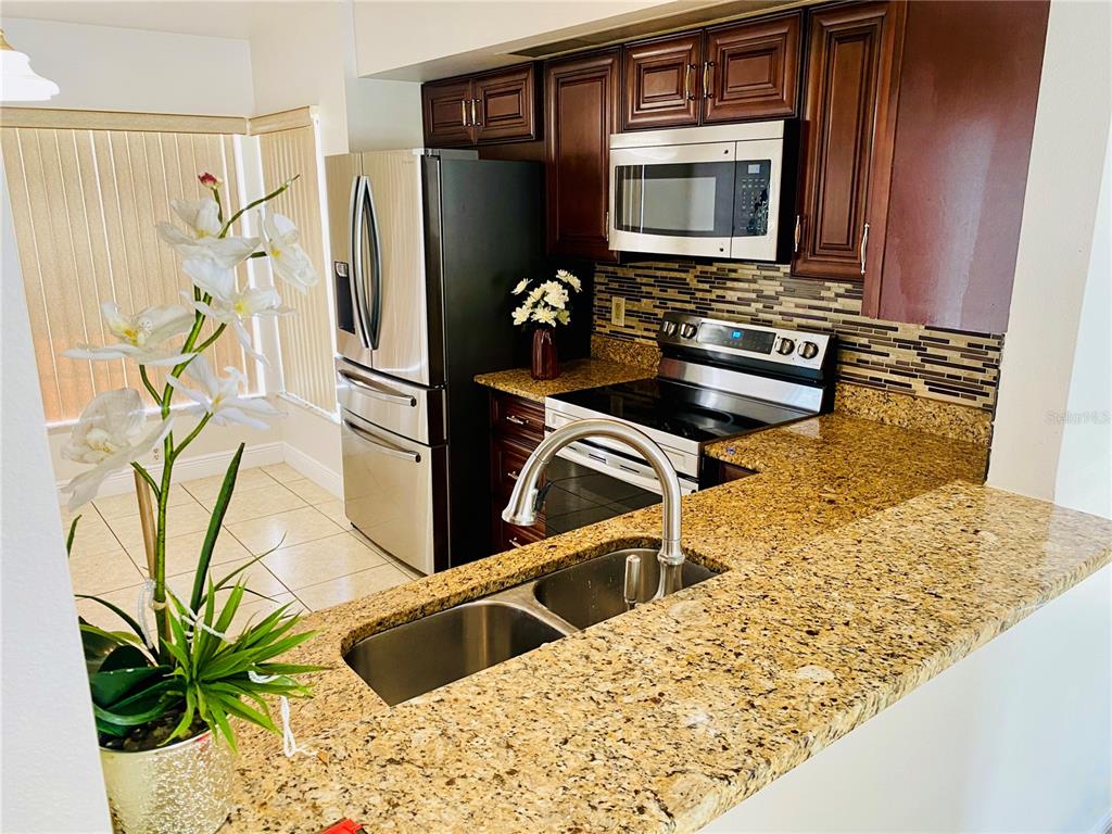 A kitchen features dark wood cabinets, granite countertops, stainless steel appliances, and a double sink — 13534 TEXAS WOODS CIRCLE, ORLANDO, FL