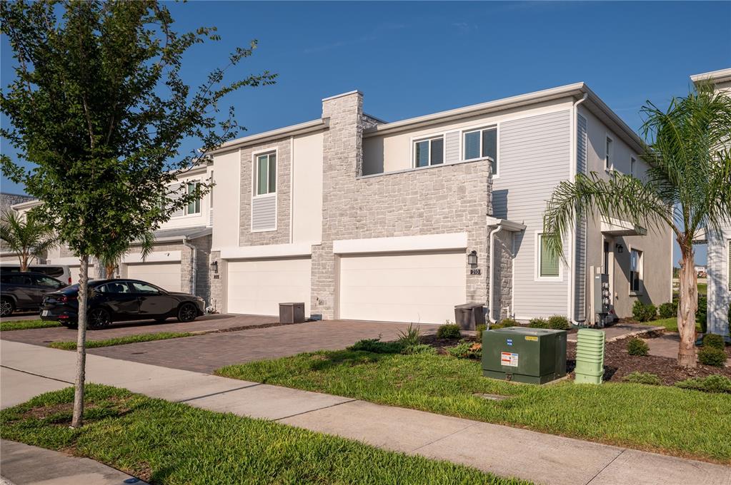 A two-story townhouse exterior features light stone veneer, gray siding, and two attached garages — 210 BOGEY DRIVE, DAVENPORT, FL