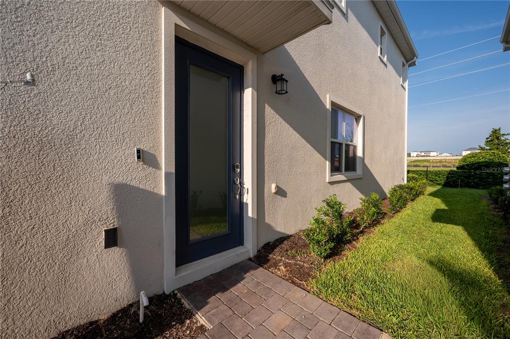 A side entrance with a dark door, a small porch, and a paved walkway — 210 BOGEY DRIVE, DAVENPORT, FL