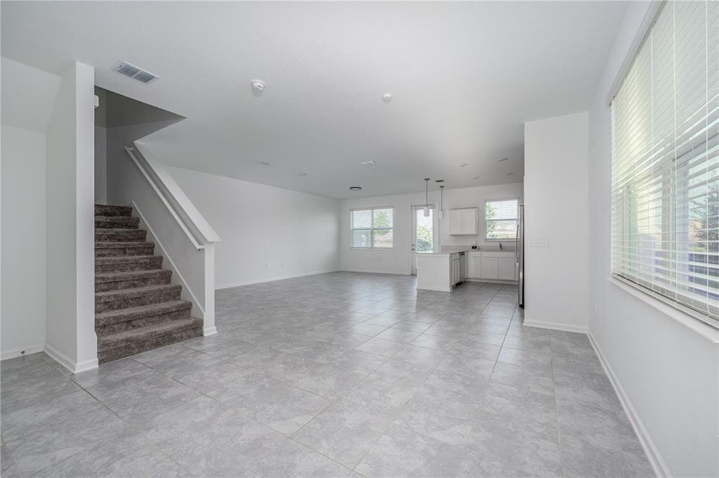 An open-concept living and kitchen area features gray tile flooring and a carpeted staircase — 210 BOGEY DRIVE, DAVENPORT, FL