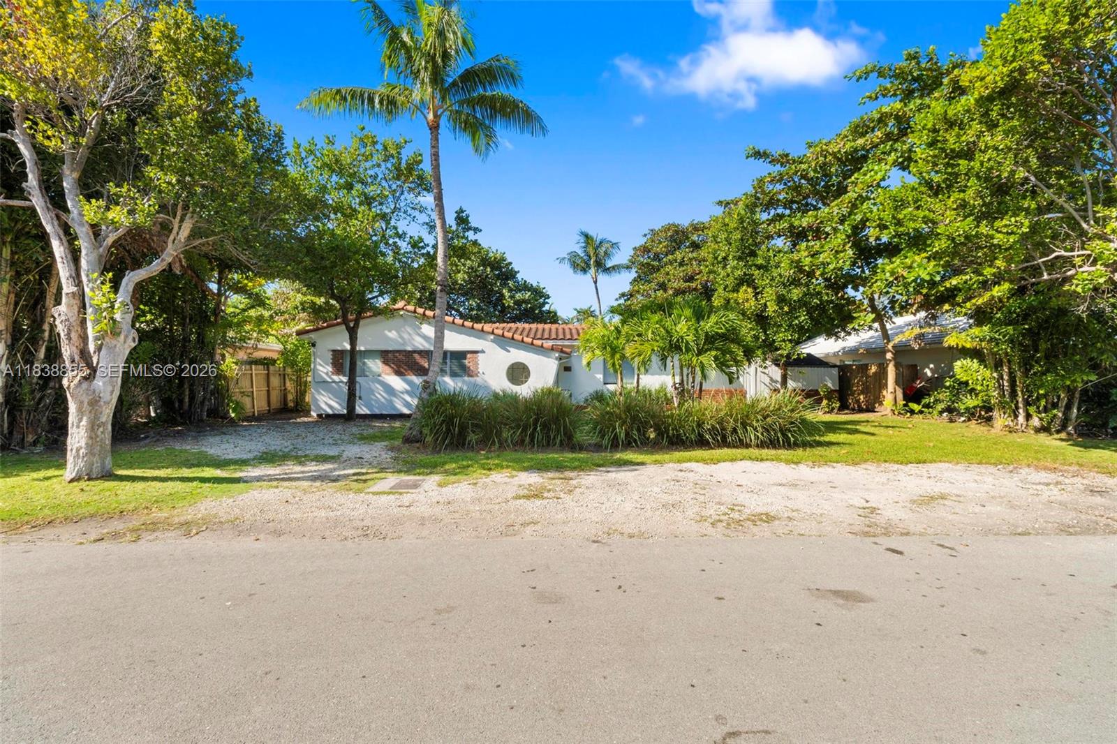 A white single-story house with a tiled roof sits behind a gravel driveway and trees — 738 Fernwood Rd, Key Biscayne FL 33149, KEY BISCAYNE, FL