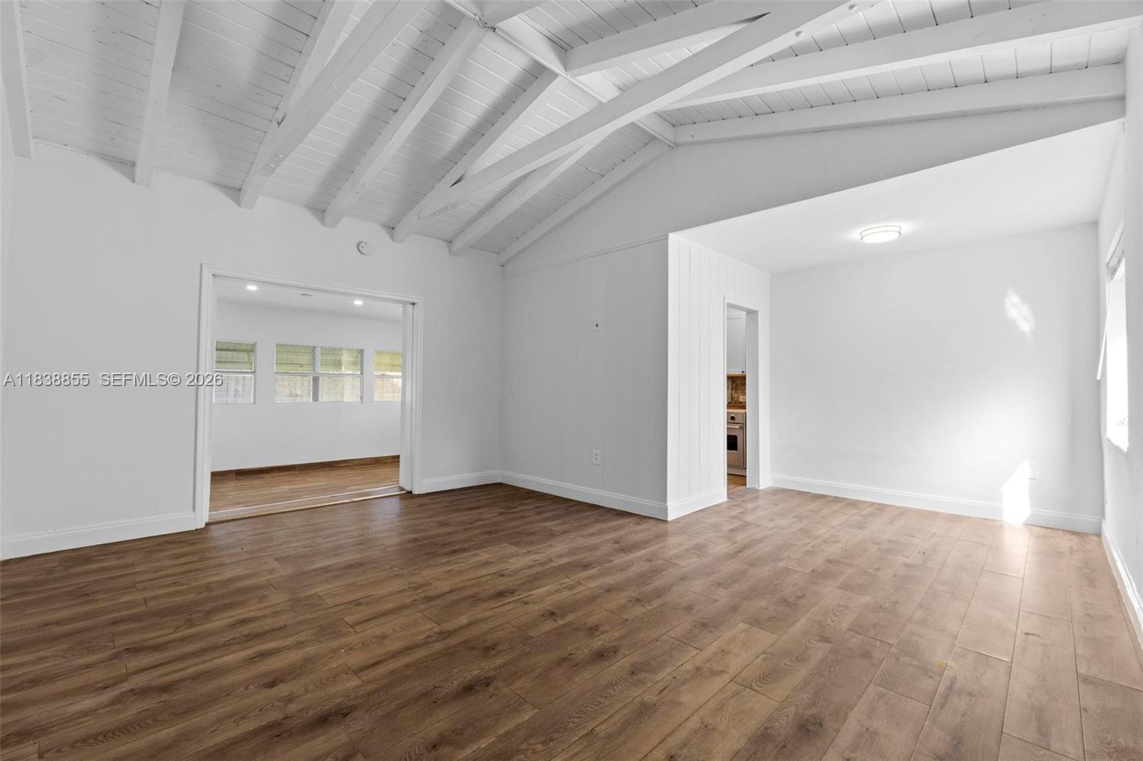 A bright living room features white vaulted ceilings, wood-look flooring, and an adjacent kitchen area — 738 Fernwood Rd, Key Biscayne FL 33149, KEY BISCAYNE, FL