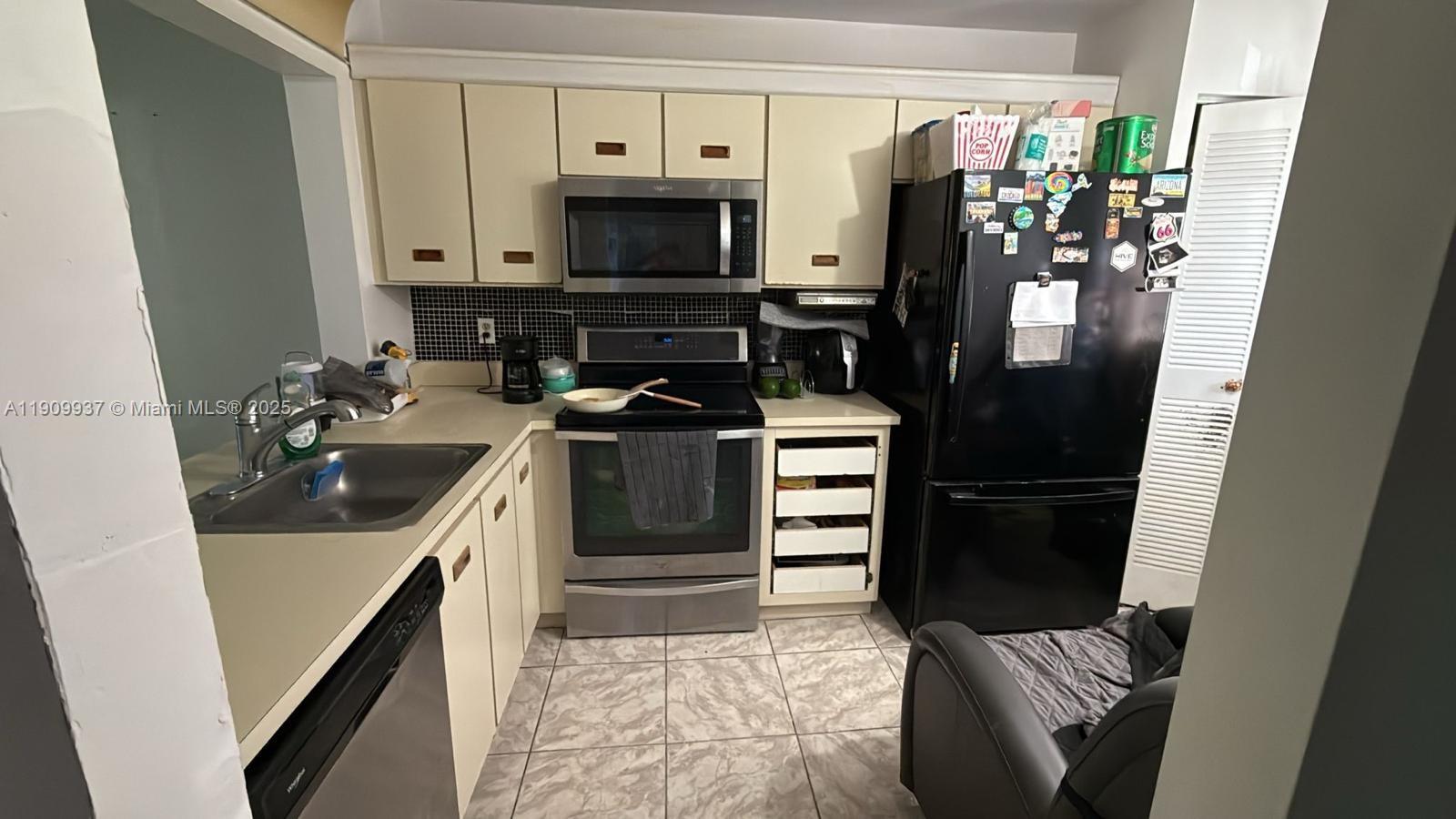 A kitchen features light-colored cabinets, stainless steel appliances, a black refrigerator, and tiled flooring — 430 NE 210th Cir Ter # 3, Miami FL 33179, MIAMI, FL