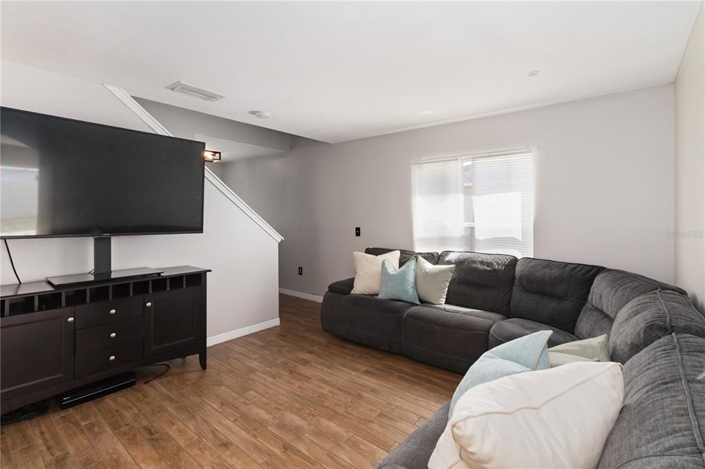 A living room features a dark sectional sofa, a television on a stand, and wood-look flooring — 7327 LUMBER PORT DRIVE, RUSKIN, FL