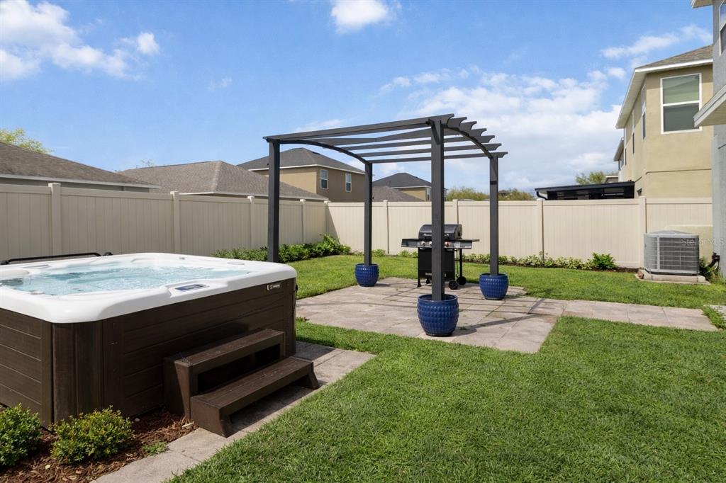 A backyard features a hot tub, a pergola over a patio, and a grill — 7327 LUMBER PORT DRIVE, RUSKIN, FL