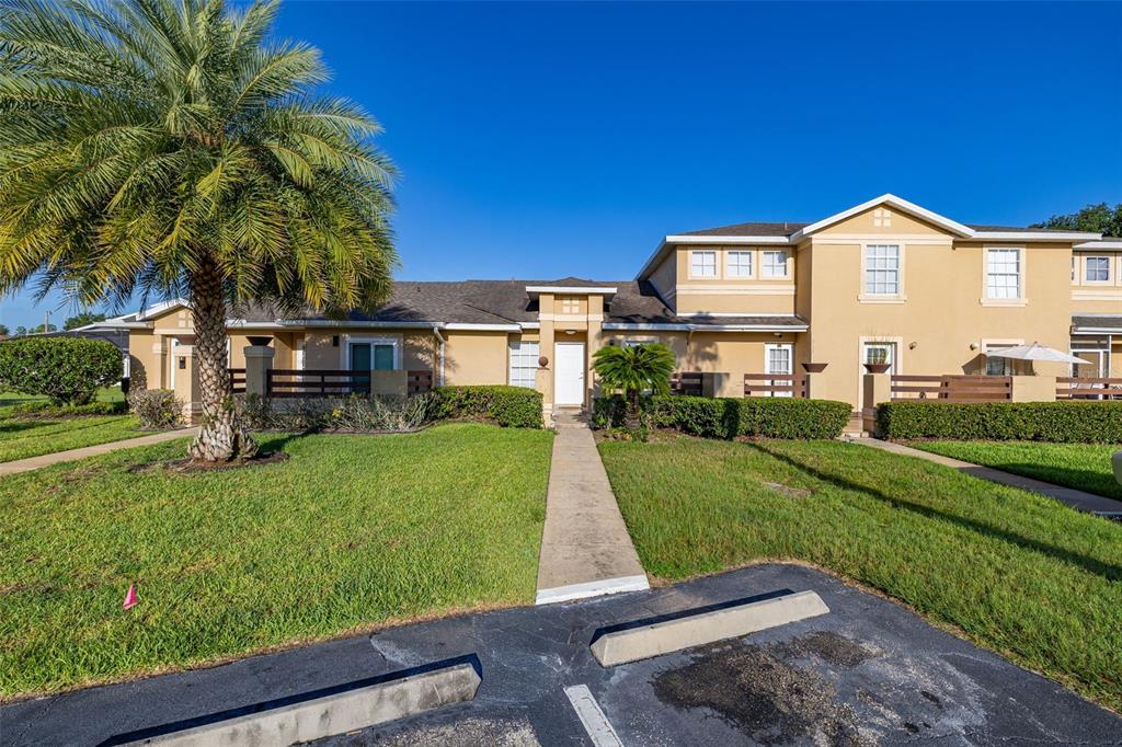 A two-story tan townhouse with a front walkway, palm tree, and parking spaces — 3128 SANDY SHORE LANE, KISSIMMEE, FL
