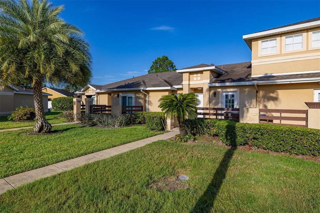 A tan townhouse exterior features a palm tree, a concrete walkway, and wooden privacy fences — 3128 SANDY SHORE LANE, KISSIMMEE, FL
