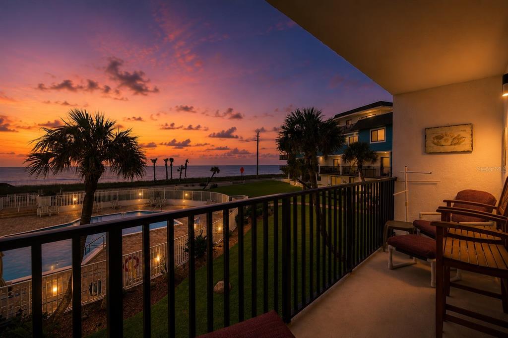 A balcony view overlooking a swimming pool, palm trees, and the ocean at sunset — 3500 S OCEAN SHORE BOULEVARD UNIT 211, FLAGLER BEACH, FL