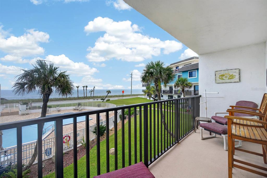 A balcony with patio furniture overlooks a swimming pool, grassy lawn, and the ocean — 3500 S OCEAN SHORE BOULEVARD UNIT 211, FLAGLER BEACH, FL