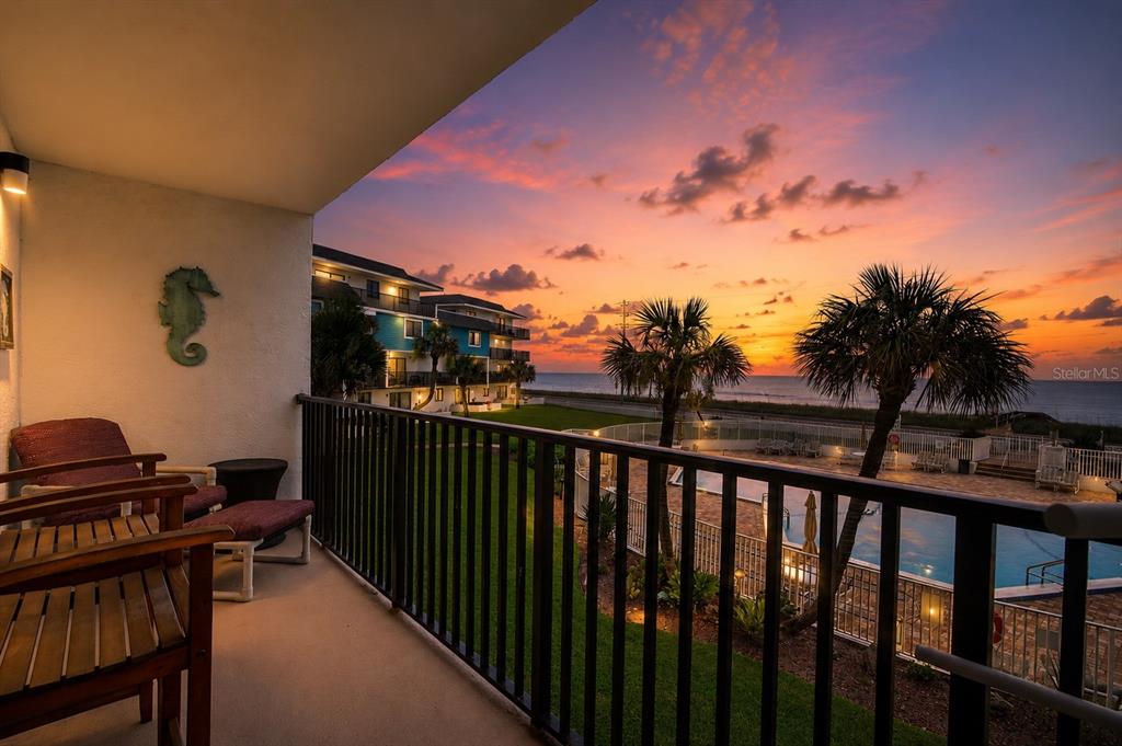 A balcony overlooks a swimming pool, palm trees, and the ocean at sunset — 3500 S OCEAN SHORE BOULEVARD UNIT 211, FLAGLER BEACH, FL