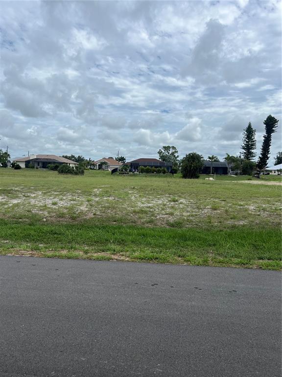 A vacant, grassy residential lot sits in front of several single-family homes under a cloudy sky — 120 MARK TWAIN LANE, ROTONDA WEST, FL