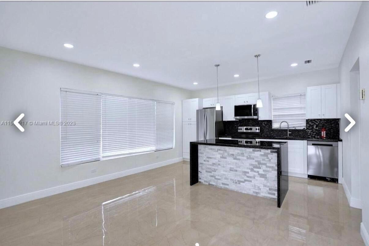 A kitchen with white cabinets, black countertops, and a stone-faced island in an open room — 6720 Coolidge Street, Hollywood FL 33024, HOLLYWOOD, FL