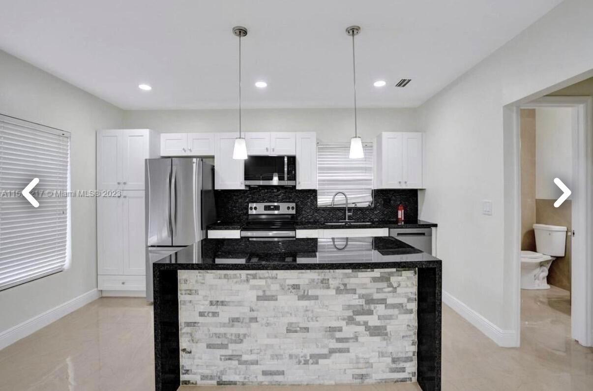 A kitchen features white cabinets, black countertops, a stone-faced island, and an adjacent bathroom door — 6720 Coolidge Street, Hollywood FL 33024, HOLLYWOOD, FL