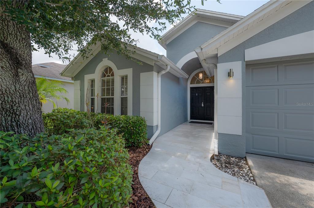 A stone walkway leads to the dark double front doors of a grey stucco house — 11820 EASTHAMPTON DRIVE, TAMPA, FL