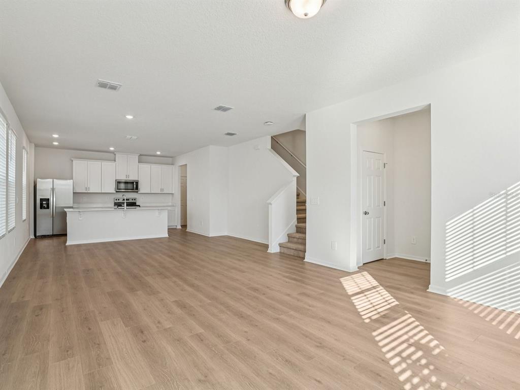 An open-concept kitchen and living area features white cabinetry, light wood flooring, and a staircase — 4685 CROSS PRAIRIE PARKWAY, ST CLOUD, FL